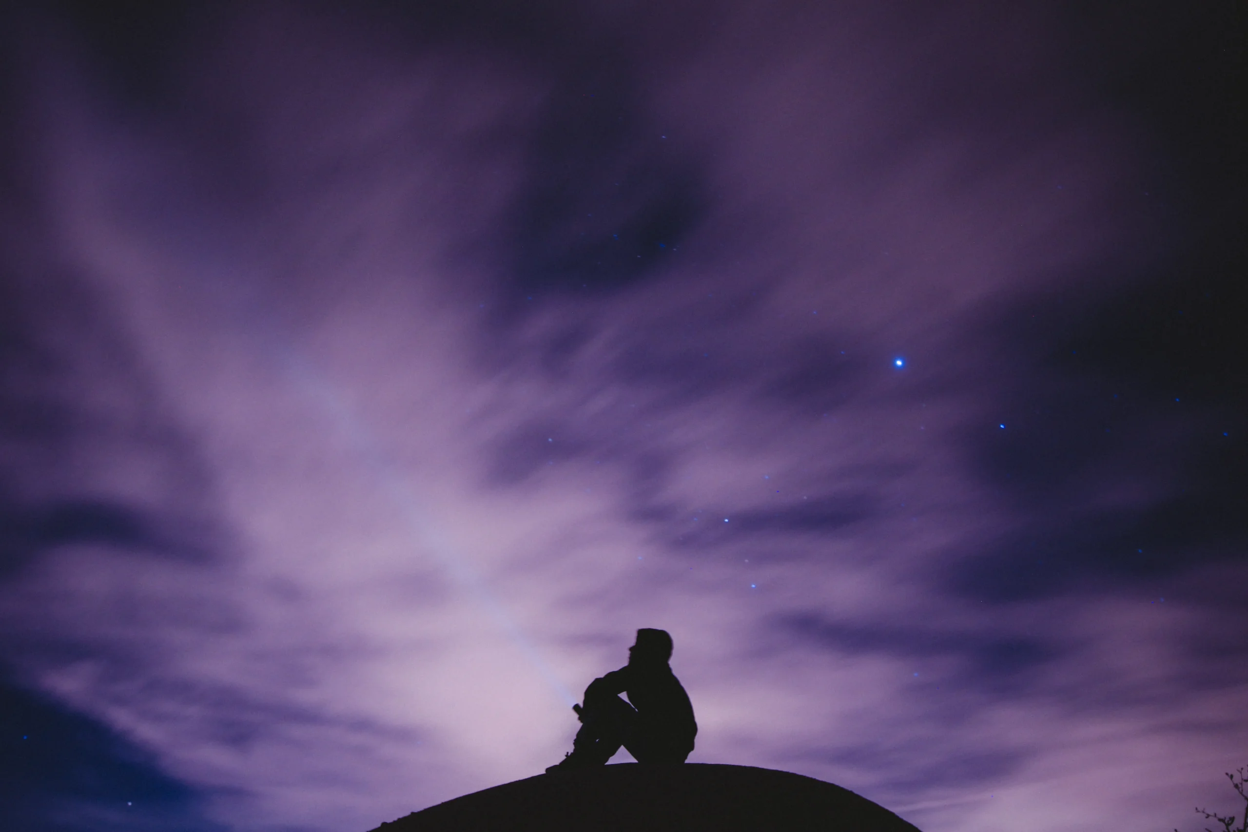 Silhouette of a person sitting on a hill Silhouette of a person sitting on a hill, looking at stars in the night sky. Credit: Photo by Jeremy Bishop on Unsplash